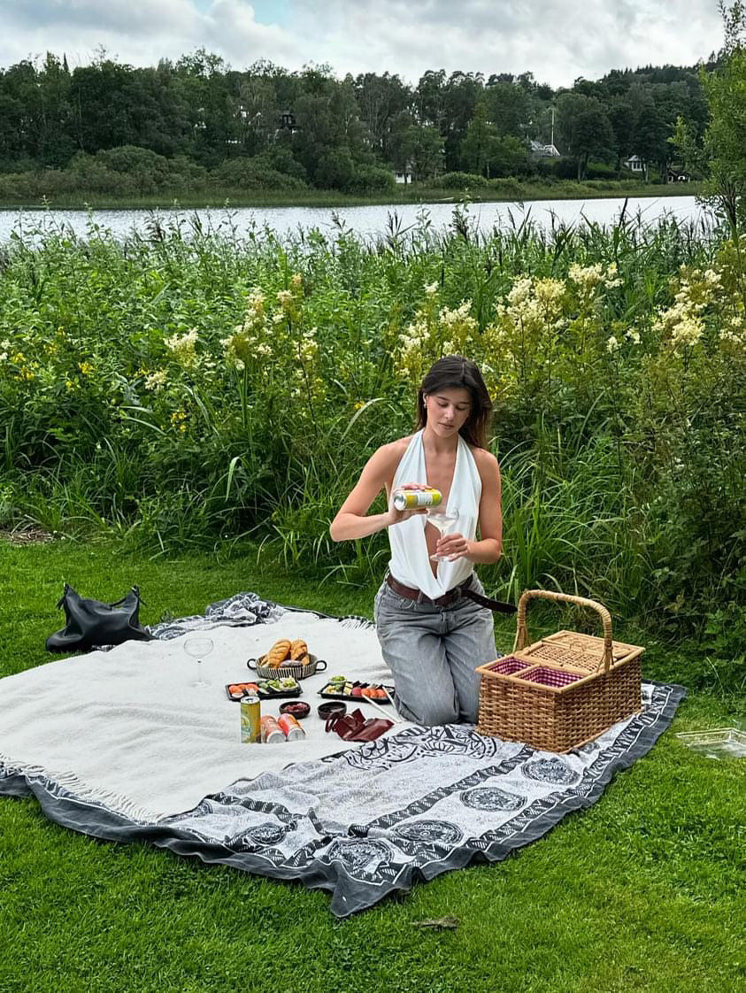 A beautiful woman enjoys a sunny picnic, pouring hÄppi prebiotic soda into a glass surrounded by flowers and healthy snacks. Perfect for outdoor gatherings, hÄppi sodas add a refreshing and gut-friendly boost to your picnic experience.