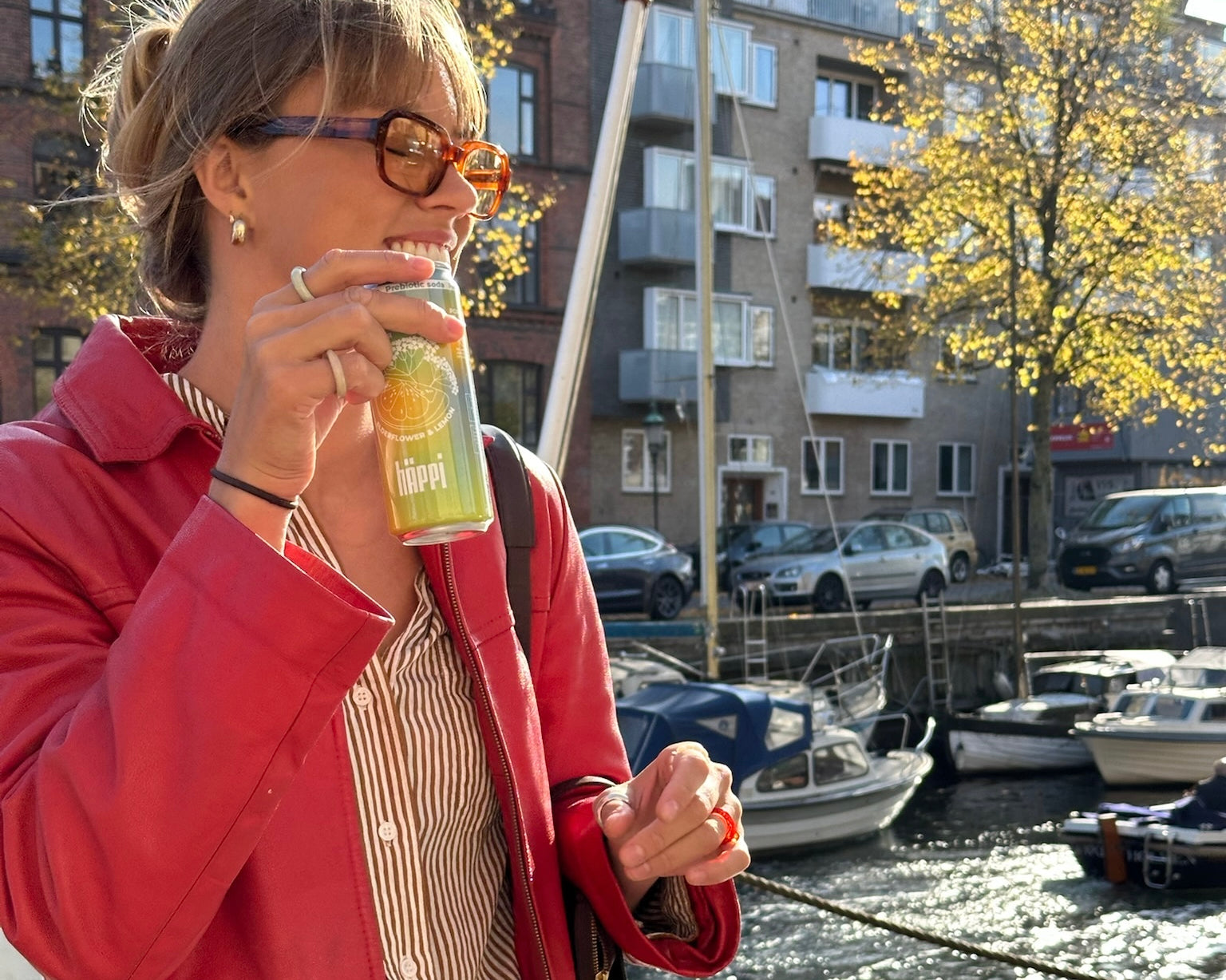 A woman enjoying a refreshing hÄppi ACV-infused prebiotic soda by the waterfront on a sunny day, embodying a natural and healthy lifestyle.