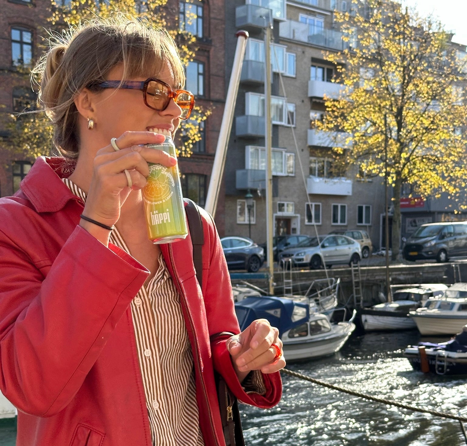 A woman enjoying a refreshing hÄppi ACV-infused prebiotic soda by the waterfront on a sunny day, embodying a natural and healthy lifestyle.